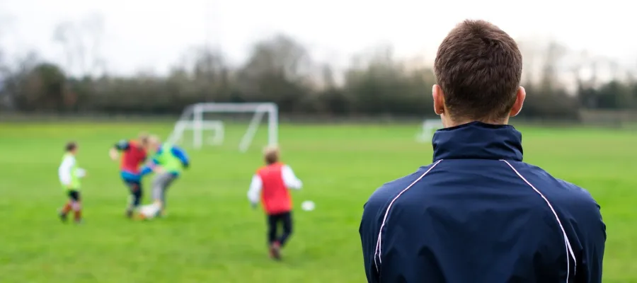 Allenatore che guarda bambini che giocano a calcio